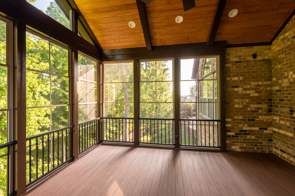 Modern screened porch enclosure with plastic windows and composite floor with summer woods in the background