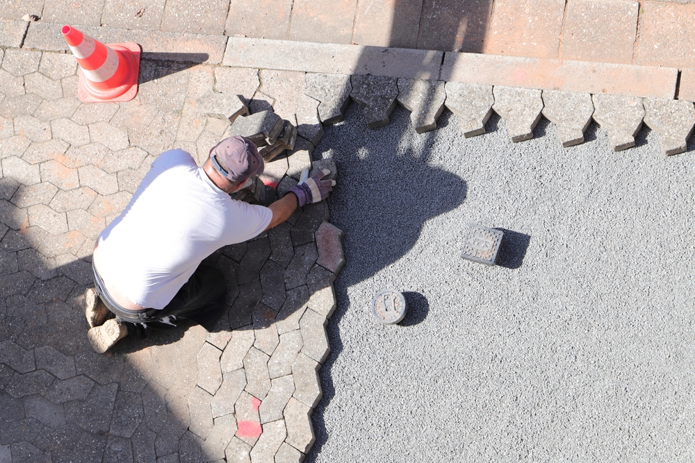Aworkerislayingpavingstonesingravel | h3 outdoor design & construction a Worker is Laying Paving Stones in Gravel