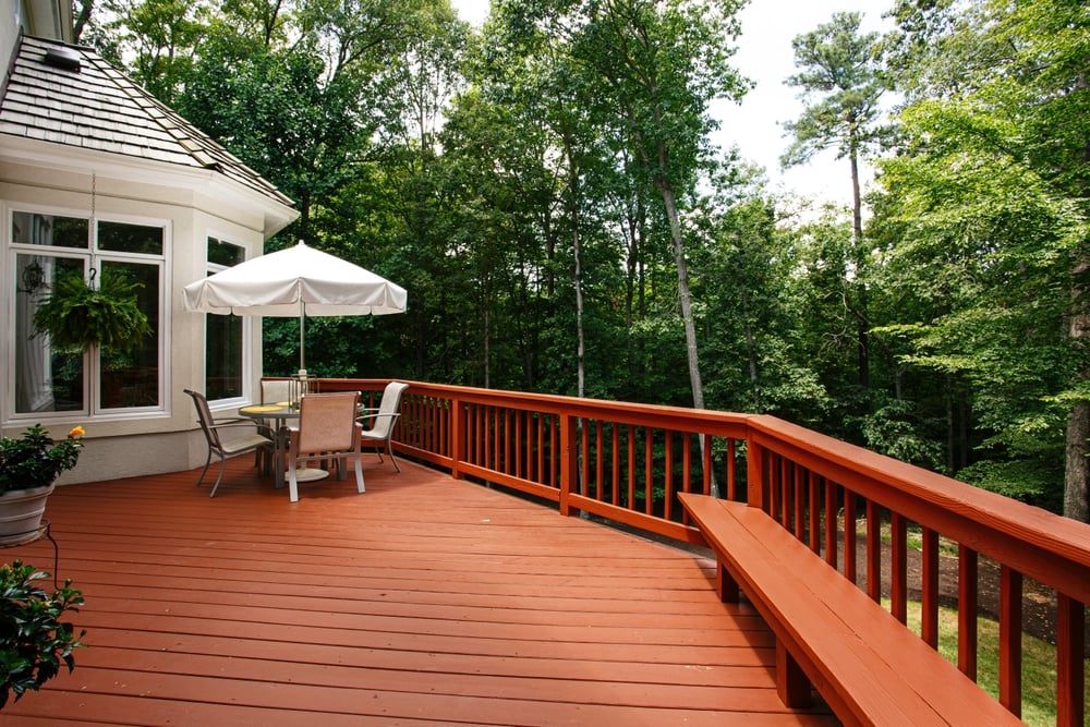 Large Wooden Deck Featuring an Umbrella-covered Outdoor Dining Set Surrounded by a Dense Forest in Summer