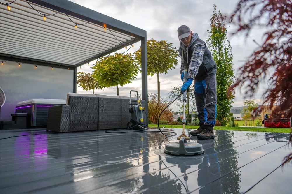 A person is cleaning a deck in a garden using a pressure washer